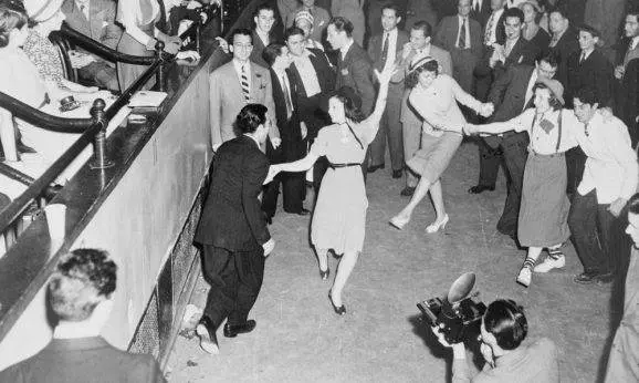 Back & White photo of men & women dancing west coast swing in a crowded dance floor and room